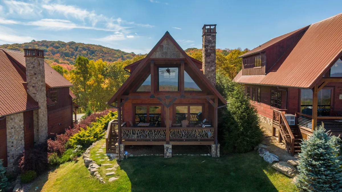 This exterior shot captures the striking A-frame architecture of Mountain Valley Lodge, complete with a stone chimney, expansive windows, and a beautifully landscaped garden. The inviting porch and lush greenery emphasize the lodge's close relationship with the natural surroundings.