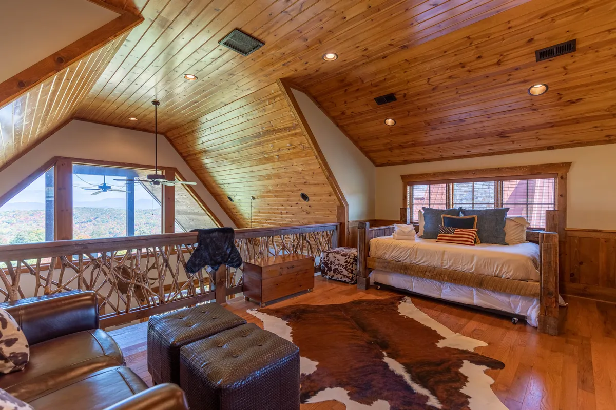 A spacious suite showcasing a wooden ceiling, large windows offering scenic views, a cozy bed setup, cowhide rug, and a comfortable seating area. The space feels inviting and contemporary with rustic touches, echoing a restful, versatile retreat.
