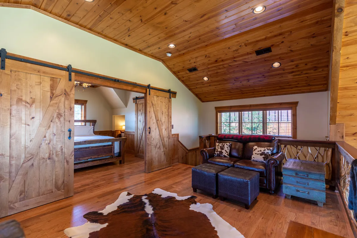 A rustic living area featuring barn doors, a leather couch, a cowhide rug, and a wooden ceiling. The barn doors evoke a sense of the outdoors and rural life, while the space feels inviting for both people and pets to relax after a day of exploration.