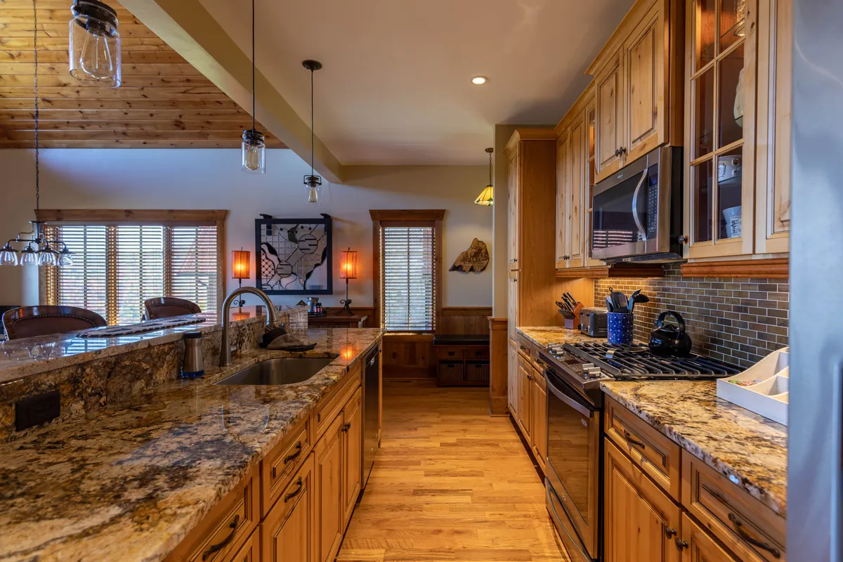 An elegant, modern kitchen with gleaming granite countertops, rich wooden cabinetry, a central island, pendant lighting, and high-end stainless steel appliances. The layout is open and inviting, perfect for cooking together or entertaining guests.