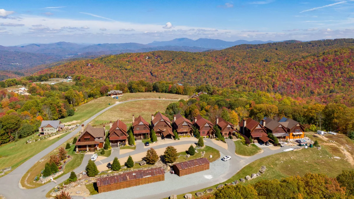 A row of charming chalets is set against a backdrop of majestic mountains and brilliant fall foliage. The communal porches and visible open areas suggest spaces where families can socialize, play, and relax, while the natural surroundings highlight opportunities for hiking and outdoor adventures.