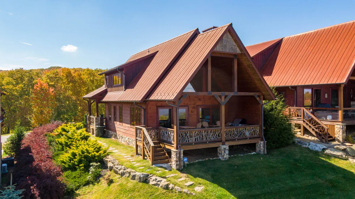 The image showcases the charming wooden exterior of Mountain Valley Lodge, framed by large windows and a spacious front porch overlooking a beautifully landscaped garden. The inviting porch hints at serene evenings spent watching sunsets and gathering with loved ones, while the surrounding natural beauty sets the scene for relaxation and outdoor adventure.