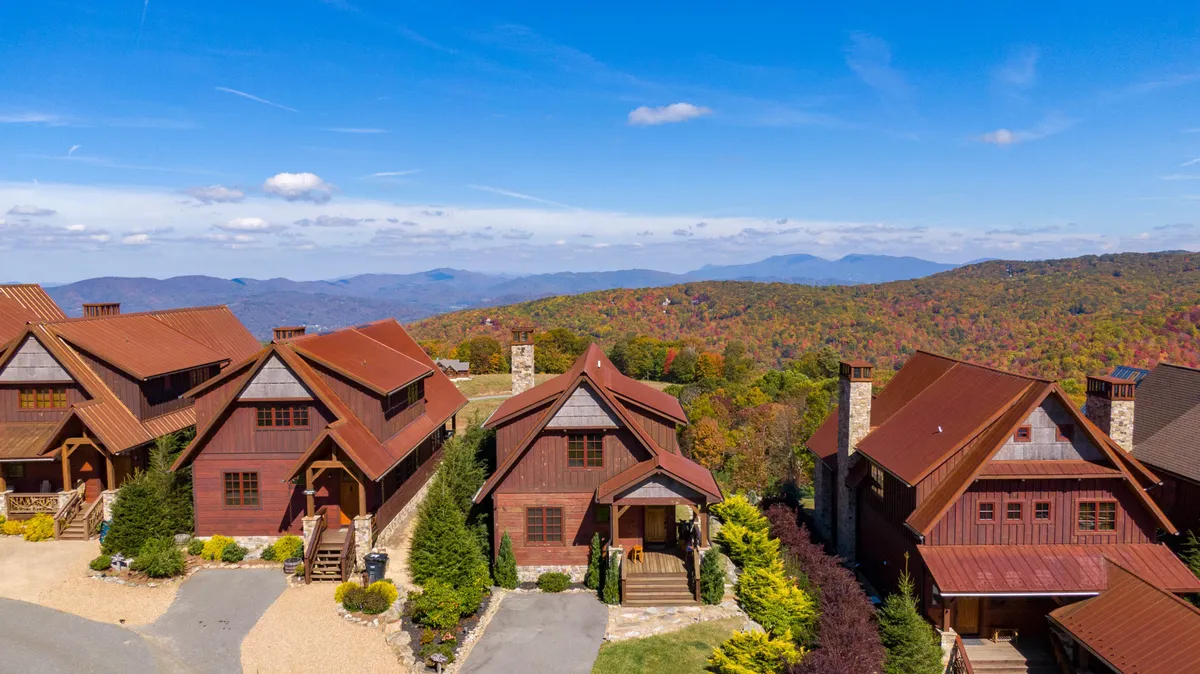 This exterior image features a sweeping view of a mountain range with vibrant, colorful foliage. Architectural details of the houses are visible, blending seamlessly into the natural landscape. The scene evokes the spirit of outdoor adventure and family connection, with an inviting porch and cozy fire pit area suggesting fun gatherings and relaxation after energetic activities.