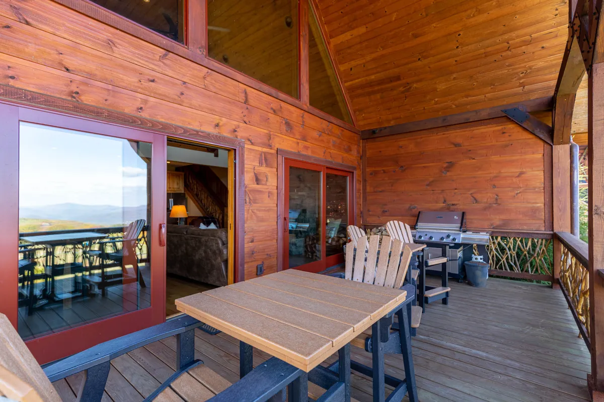 A welcoming deck scene with wooden furniture and a grill, offering panoramic views beyond the railing. The image suggests gatherings for outdoor dining, morning coffee, or lively dinners under the stars, all with a stunning mountain backdrop.